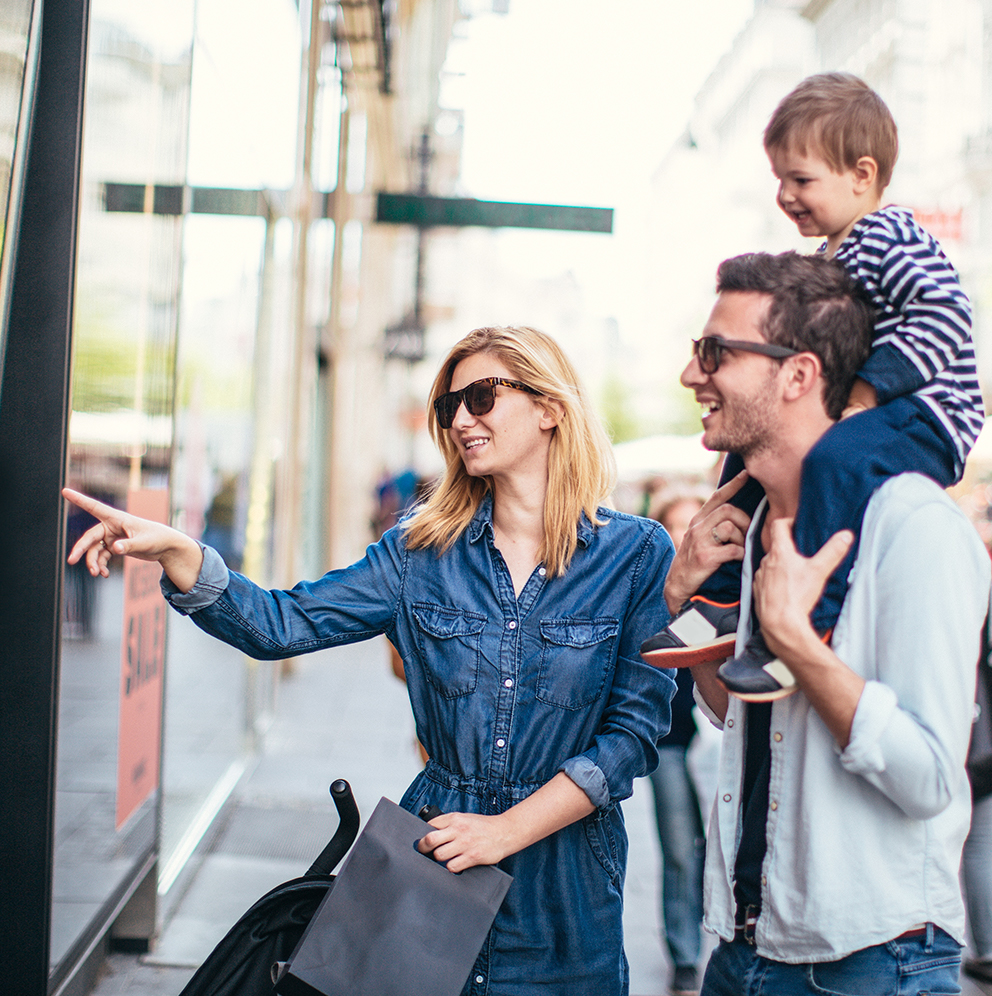 Familie beim Einkaufsbummel in der Stadt, lachend und entspannt vor einem Schaufenster.